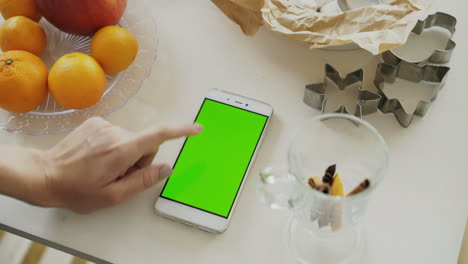 person using a smartphone with a green screen, surrounded by christmas baking ingredients