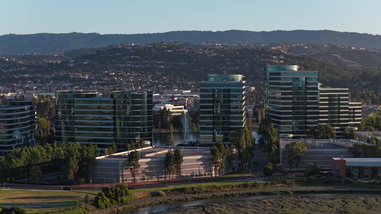 Filmato da drone all'ora d'oro che sorvola il campus della sede centrale di Oracle a Redwood Shores, rivelando i moderni edifici in vetro, il lago centrale e il paesaggio circostante della Silicon Valley.