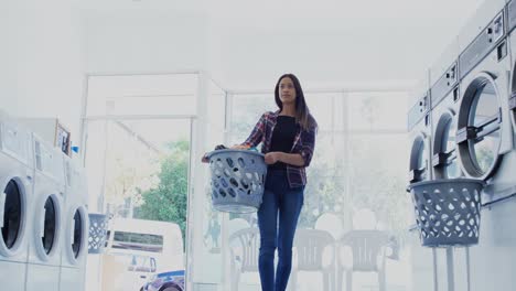 Woman-carrying-clothes-in-laundry-basket-at-laundromat-4k