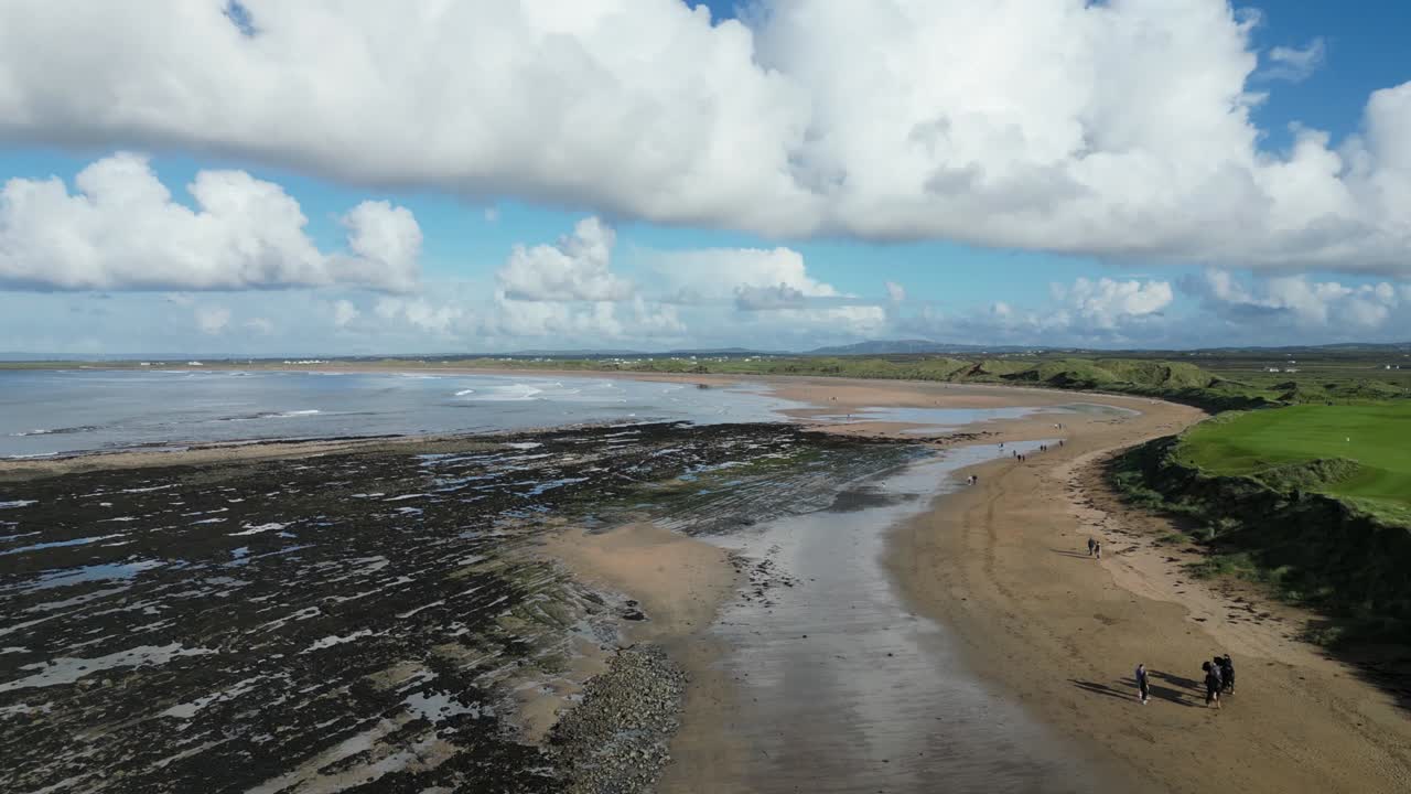 la bahía de doughmore con una extensa playa, aguas azules y un campo verde bajo un cielo lleno de nubes, vista aérea