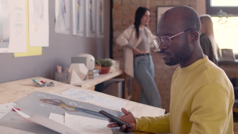 hombre enfocado tomando fotos de bocetos con teléfono móvil mientras se sienta en el escritorio de dibujo en un estudio de animación
