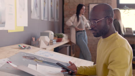 focused man taking photo of sketches with mobile phone while sitting at drawing desk in an animation studio