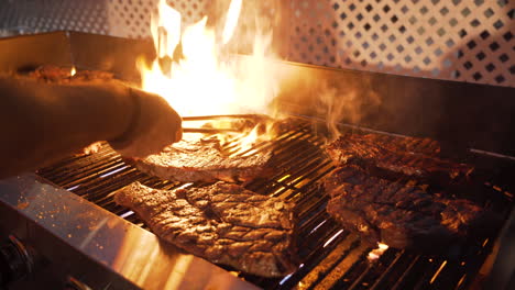 many large tasty steaks grilled over the hot fire of a grill with large brilliant flames dramatic at night