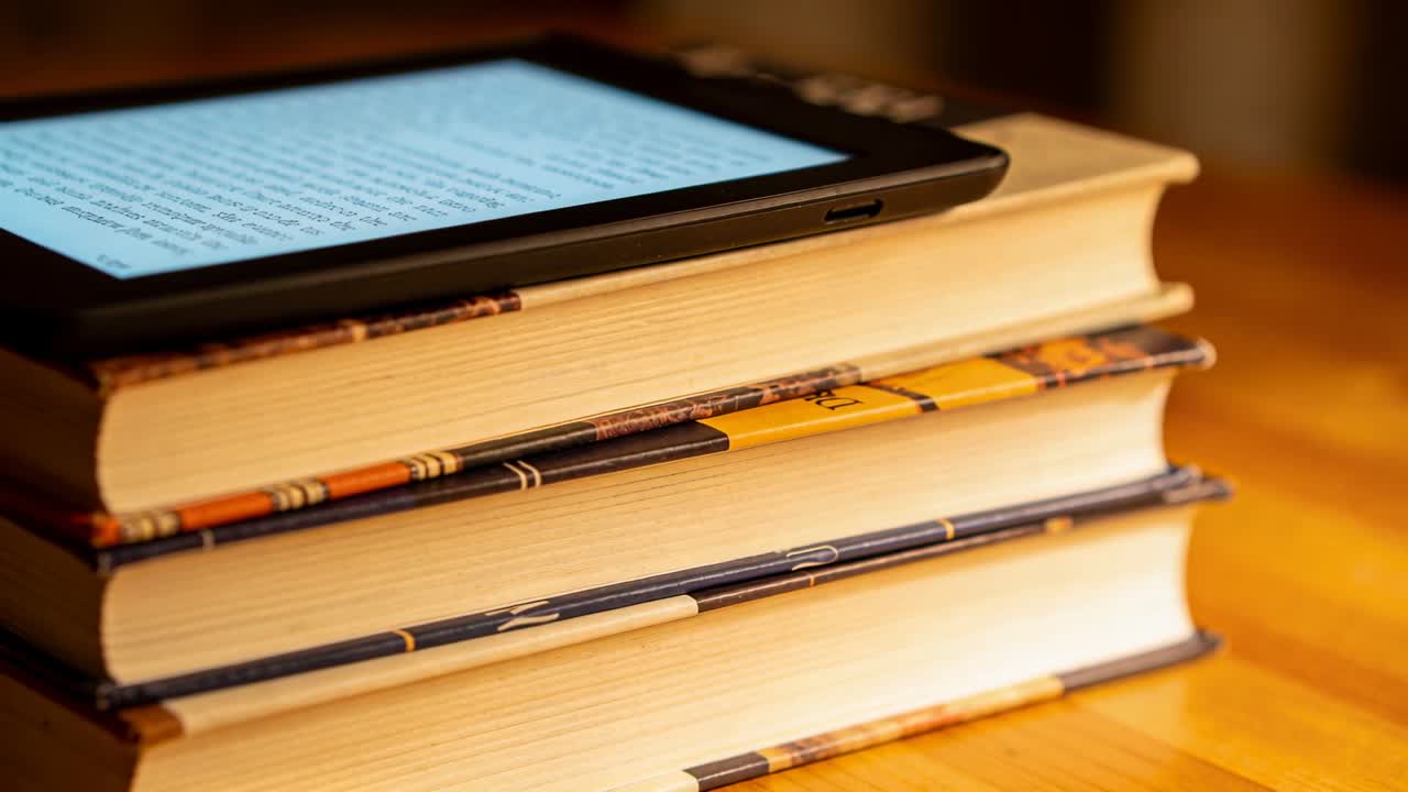 Tightening camera frame shifting focus on wooden table, revealing e-reader and hardcover books