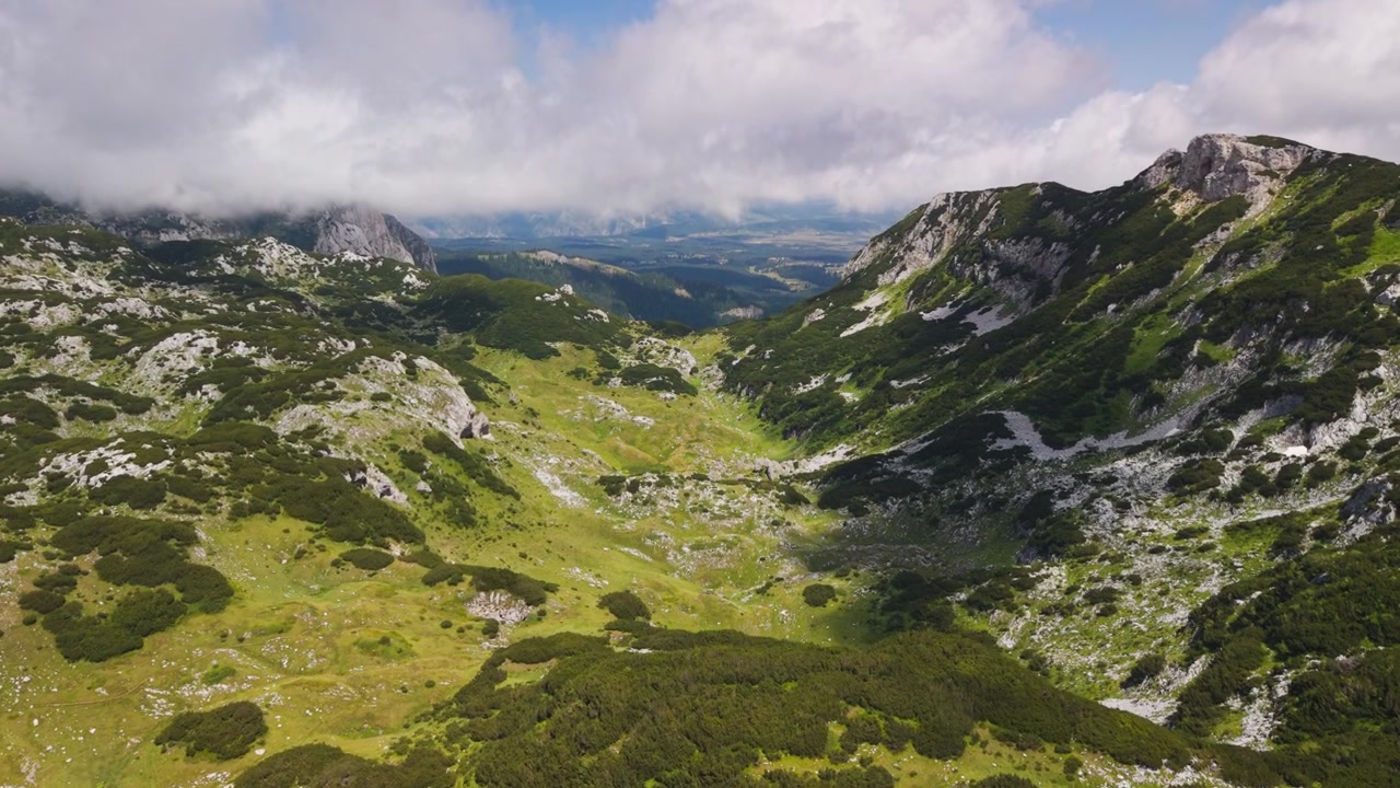 Højt luftfoto af en grøn alpedal omgivet af klippetoppe og lave skyer i Durmitor Nationalpark, Montenegro