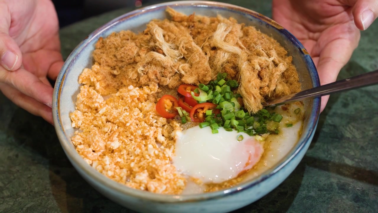 Tampak dekat bubur nasi gurih dengan taburan abon babi, telur, dan daun bawang di atas meja