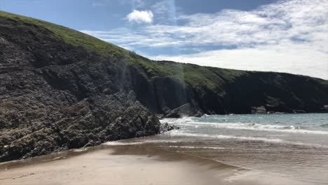 Sandy-beach-in-Wales-in-front-of-rugged-rocky-coastline-in-Cardigan-Bay-looming-above