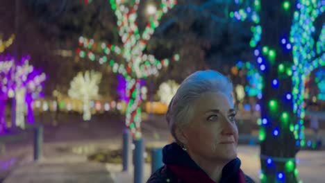 Mujer-Mayor-Caminando-Por-La-Noche-En-Una-Ciudad-Decorada-Con-Brillantes-Luces-Navideñas