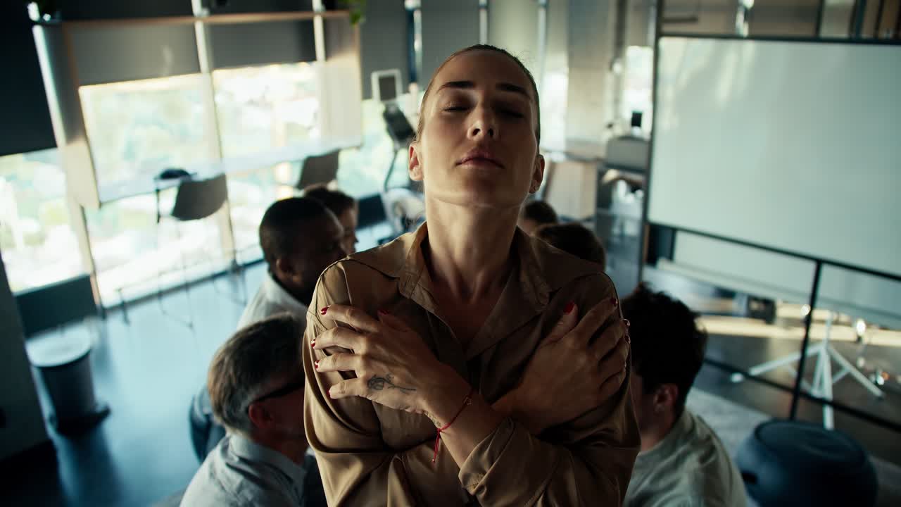 A blonde girl stands on a hill against the background of her colleagues. Trust test, the girl is tense before falling into the arms of her colleagues
