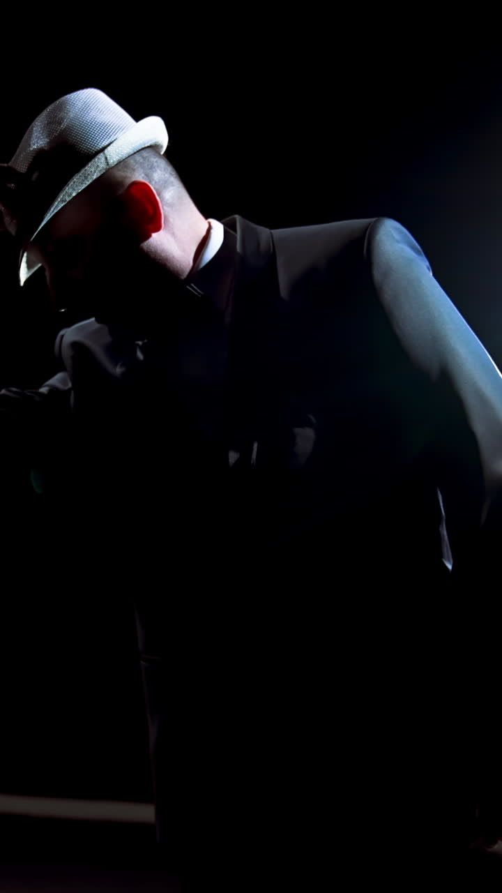 Actor making a performance on theater stage. Man in black suit putting on his hat and began dancing in darkness against spotlight. Vertical video