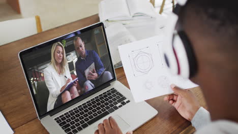african american businessman sitting at desk using laptop having video call with colleagues