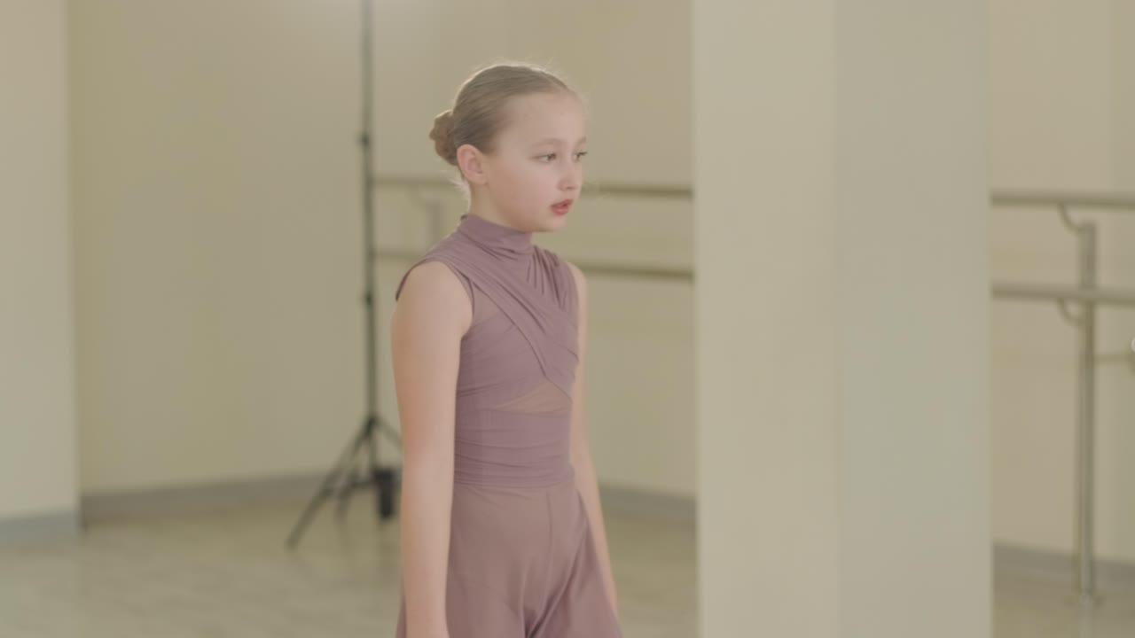 검은색 댄스웨어를 입은 젊은 발레 학생들이 나무 바닥과 벽에 장착된 바를 가진 넓은 발레 스튜디오에서 자세를 연습하는 그룹.