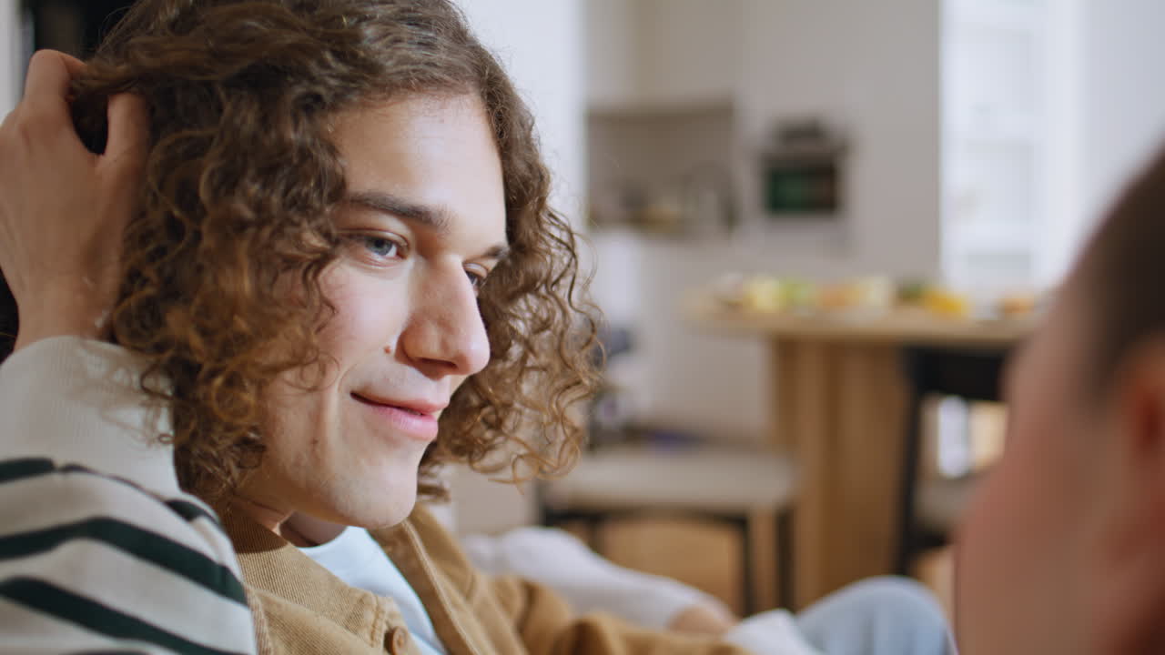 Girlfriend hand caressing hair curly boyfriend sitting at home couch closeup