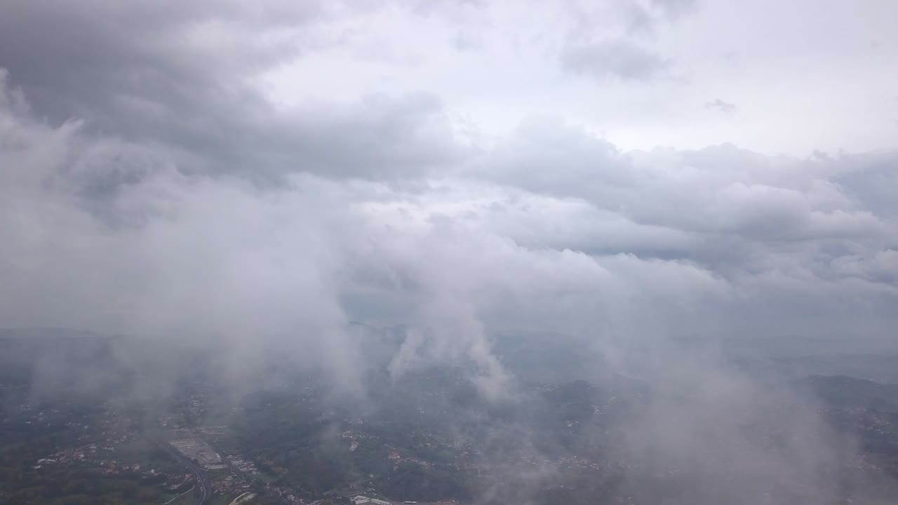 Video from above. Aerial view of a drone flying through some clouds. Italian countryside on background
