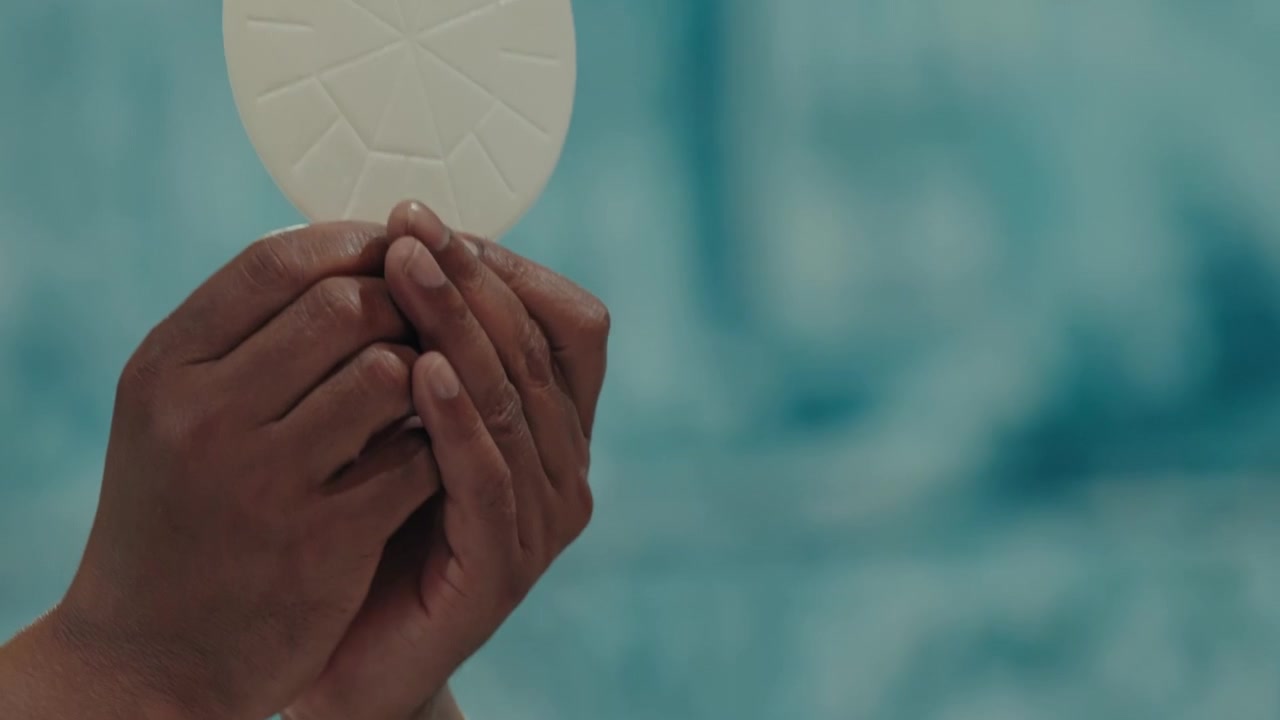 Priest in white vestments raising communion host during the Eucharist at Mass