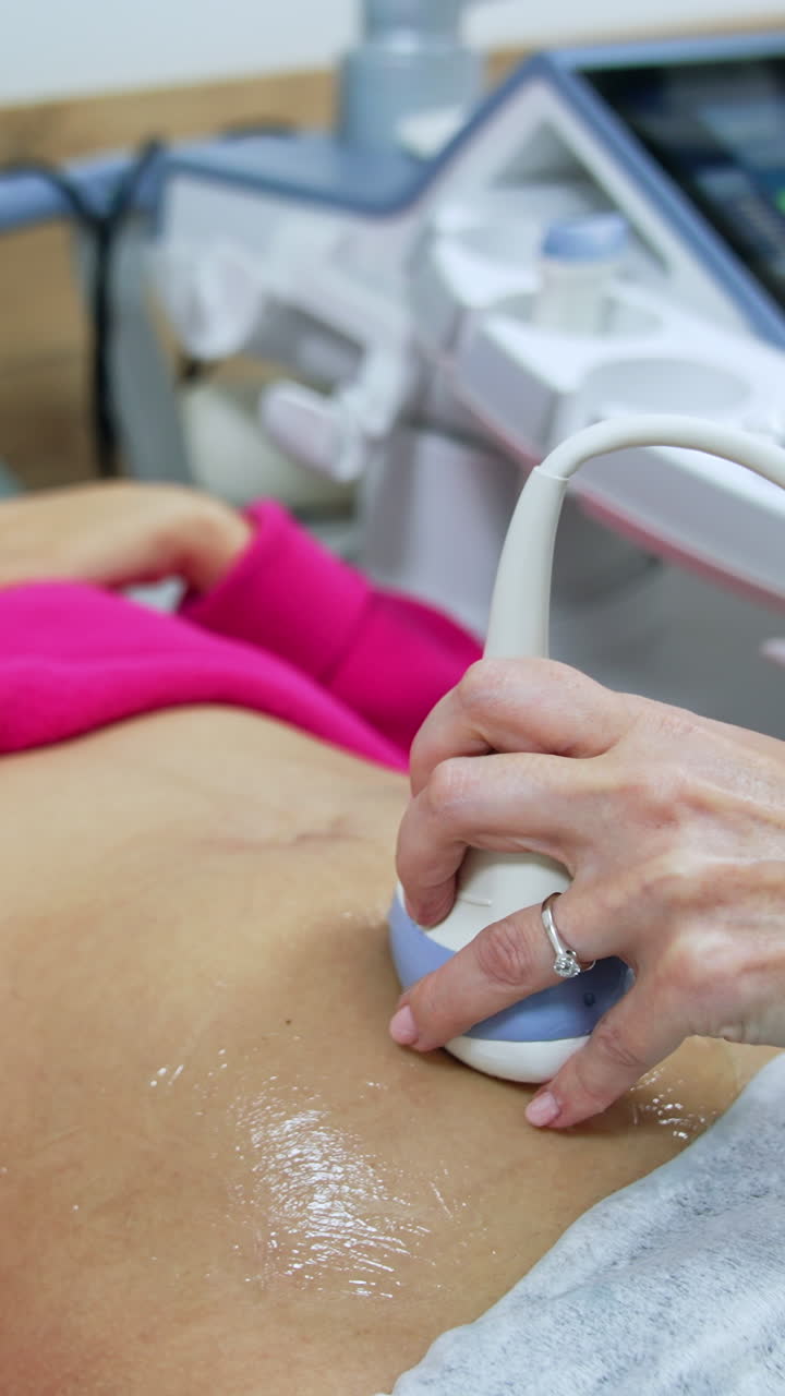 Doctor moves the transducer by the belly of blonde Caucasian woman. Future mom having pregnancy check up at ultrasonic equipment.. Vertical video