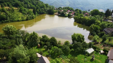 Nucsoara-lake-by-the-village-with-lush-greenery-and-quaint-houses,-daytime,-aerial-view