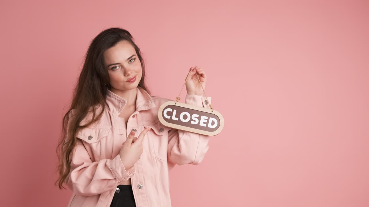 Giovane donna turbata con un cartello 'chiuso' in uno studio rosa.