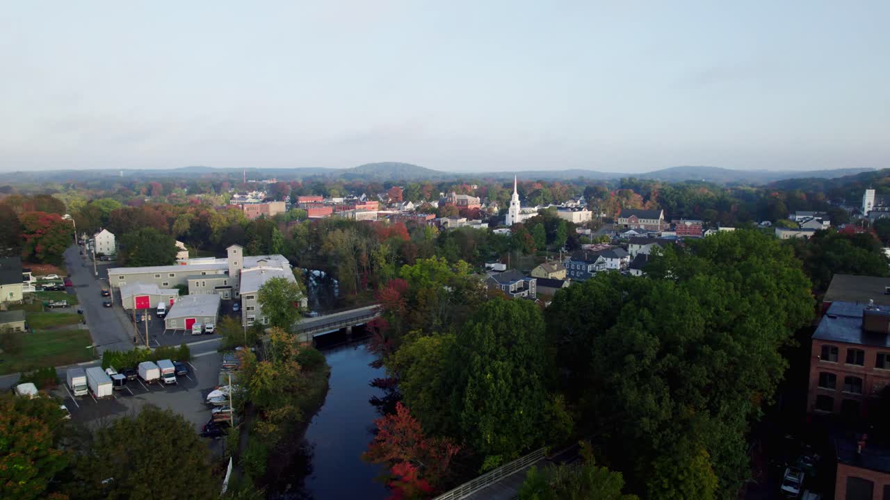 Vista aérea panorâmica enevoada do amanhecer dourado de um antigo moinho e rio nos arredores do centro de uma pequena cidade da Nova Inglaterra em Hudson, Massachusetts.