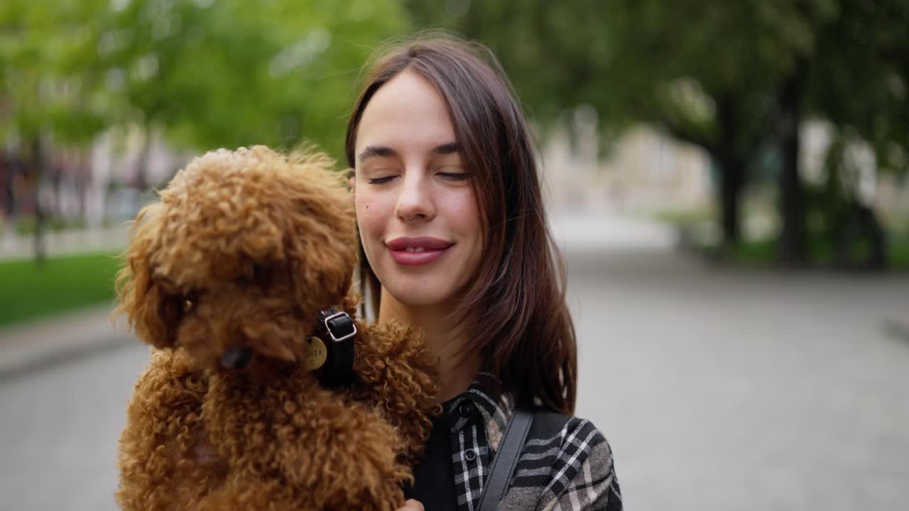 mujer sonriendo y besando a su perro caniche marrón en el parque