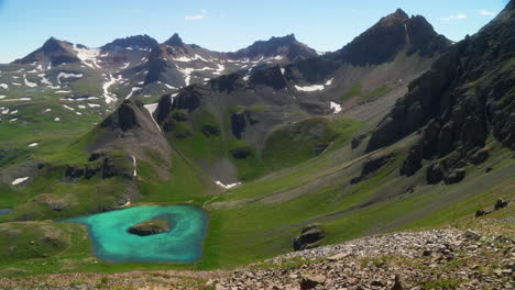 vista aérea cinematográfica superior cuenca del lago de hielo isla de silverton lago aqua azul agua clara tundra alpina impresionante cordillera nieve flores silvestres mediados del verano durante el día hermoso movimiento lento a la izquierda