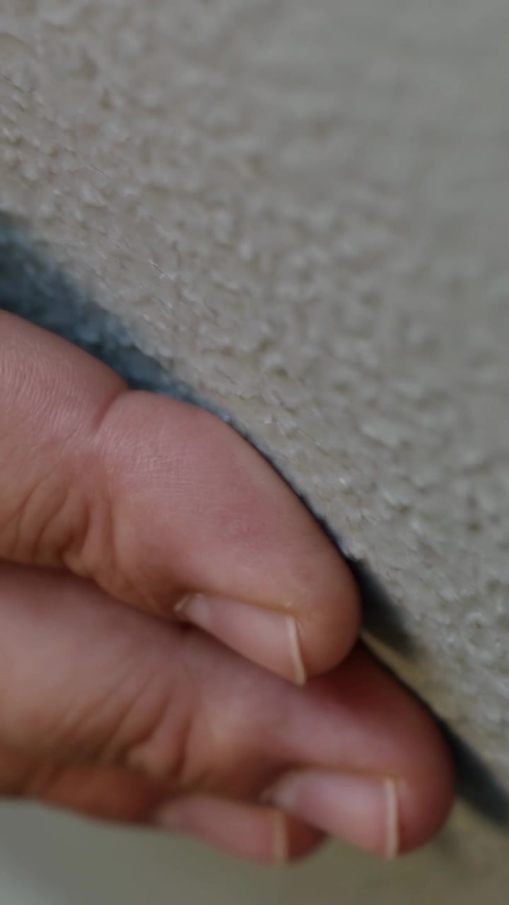 Fingertips approaching narrow textured wall seam, pressing and sliding while inspecting gap depth