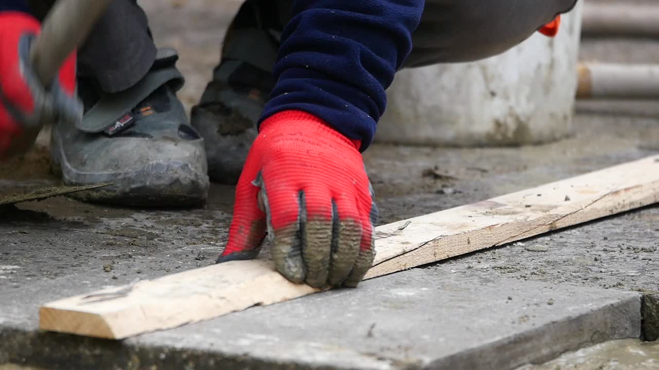 Operaio che conficca chiodi in una tavola di legno su terreno in cemento