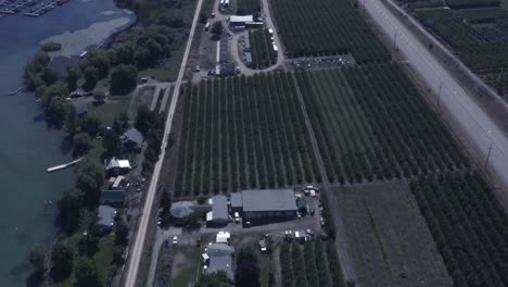 Panorámica-Aérea-Caída-Sobre-Cabañas-Muelles-Junto-Al-Lago-Lanchas-Ancladas-A-Lo-Largo-De-La-Autopista-Viñedos-Plantas-De-Procesamiento-De-Vino-Tiendas-Minoristas-Camino-De-Tierra-En-Un-Día-De-Verano-Caluroso-Y-Brumoso-Con-Casas-Transparentes-Frente-Al-Mar-3-4