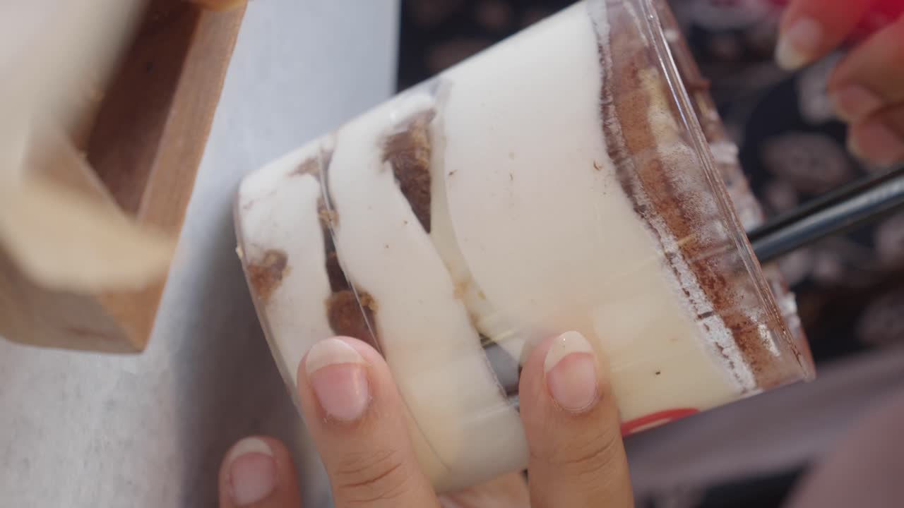 Hand holding a Tiramisu dessert in a glass cup