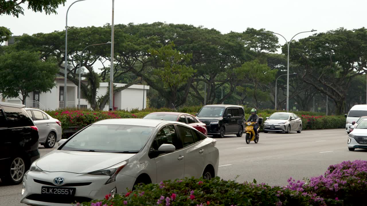 Bidikan lebar mobil, truk, dan sepeda motor yang melakukan perjalanan di jalan raya kota tropis pada siang hari