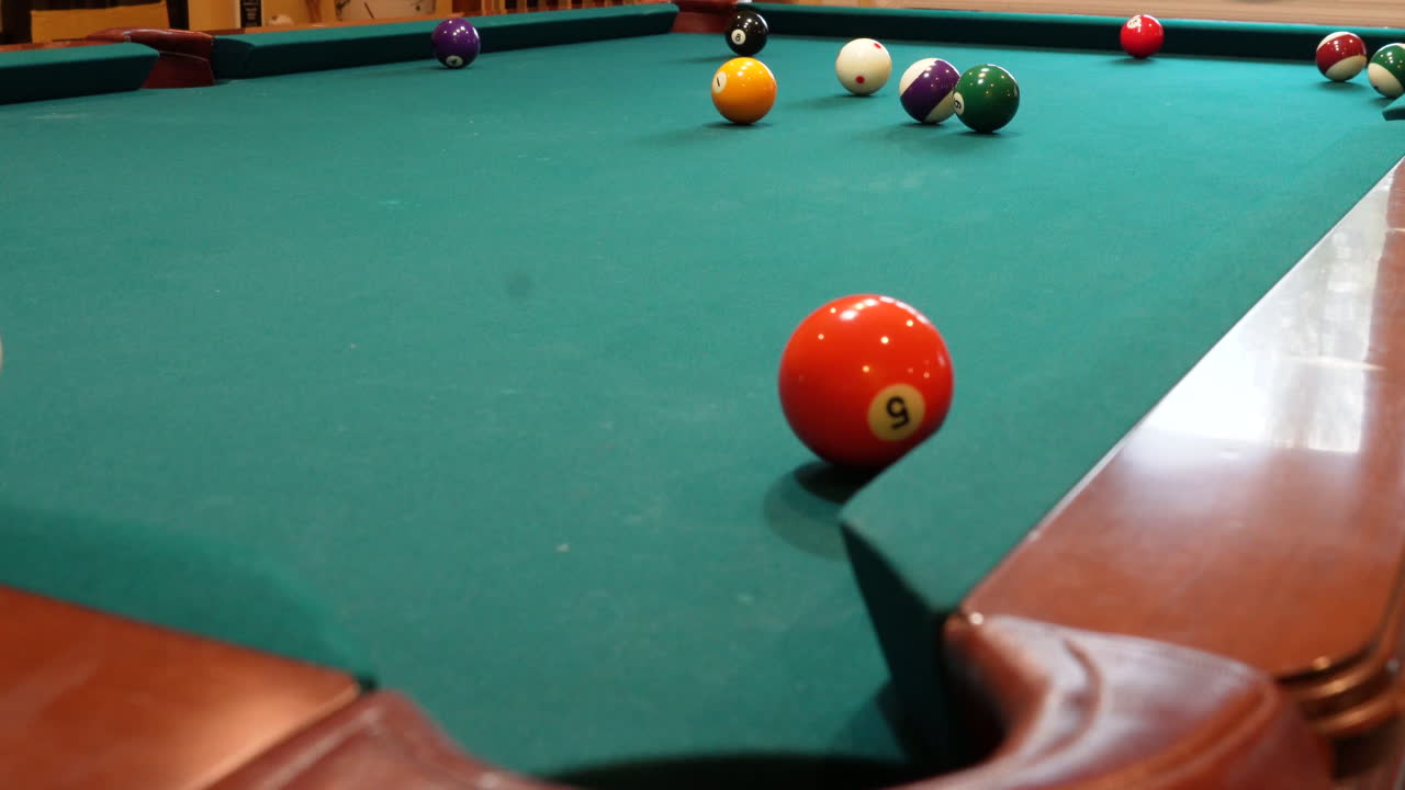 Man Playing 8 Ball Pool Shoots Several Striped Balls into Pockets on a Brunswick Table with Green Felt Missing a Shot at the End, Open Bridge Hand and Wooden Cue Stick, Low Angle