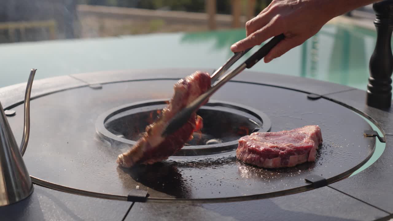 Slow motion shot of a chef flipping the steaks to evenly cook on a bbq