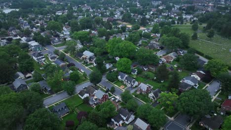 row of one family houses in neighborhood with green trees in summer. aerial top down shot. suburb residential area of town at dusk. cloudy day in june