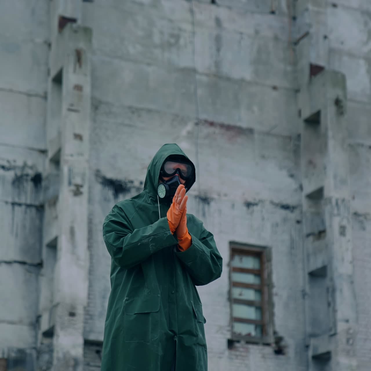 Man in protective suit and mask in infected zone. Person wearing respirator and safety uniform, in protective gloves standing on the background of abandoned building