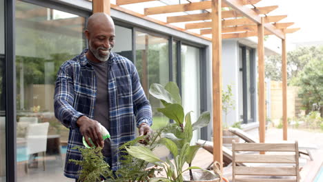 Happy-mature-african-american-man-watering-plants-on-garden-terrace,-slow-motion