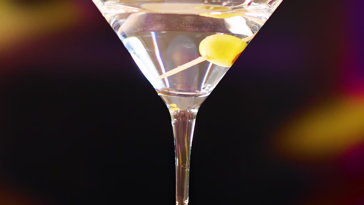 A detailed view of a martini glass featuring a lemon garnish against a dark, colorful background.