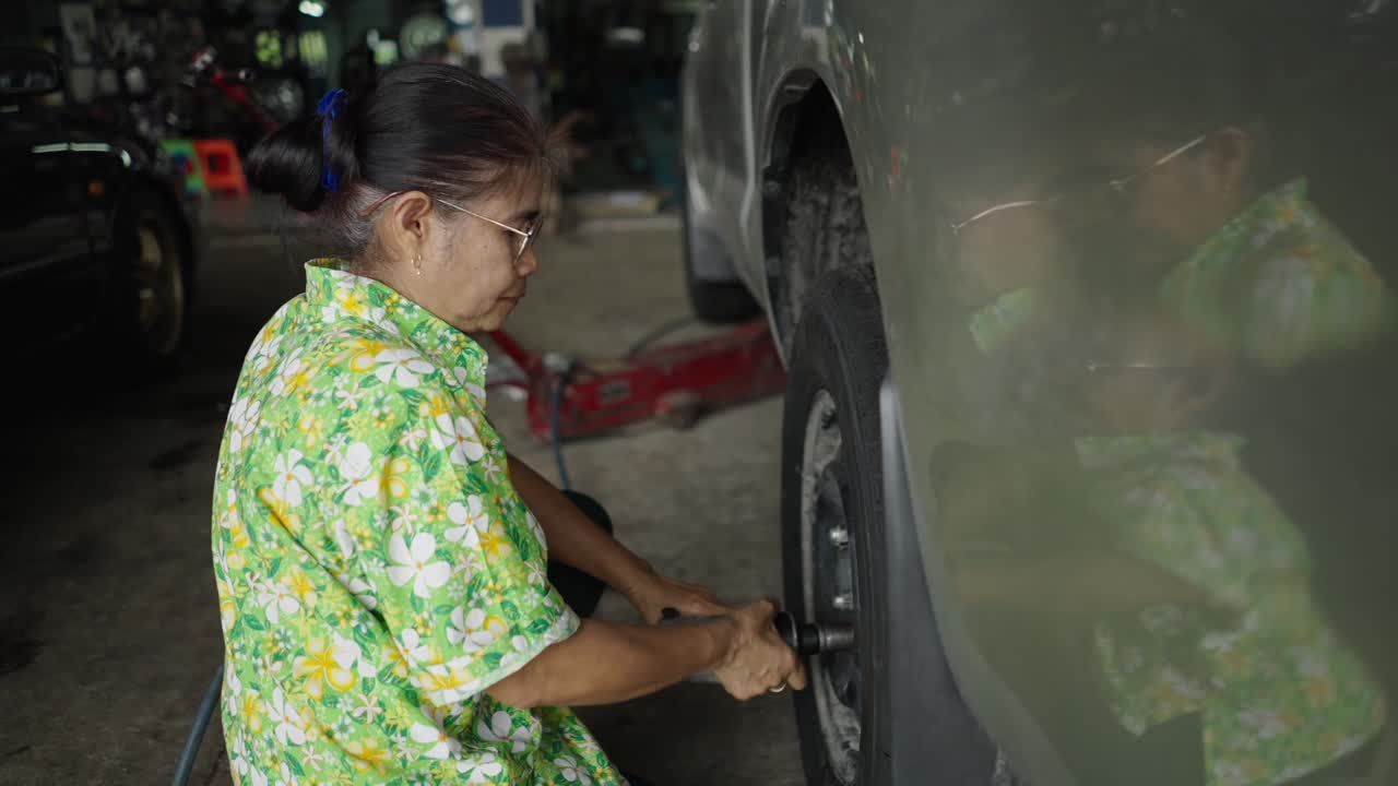 An elderly woman working on a car tire in an auto repair shop