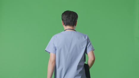 back view of asian male doctor with stethoscope holding a tablet while walking on green screen background in the hospital