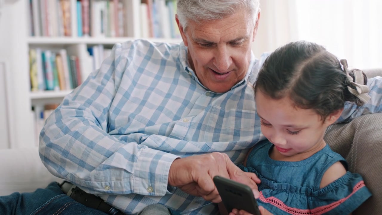 Grandfather and Granddaughter Using Smartphone Together on Sofa