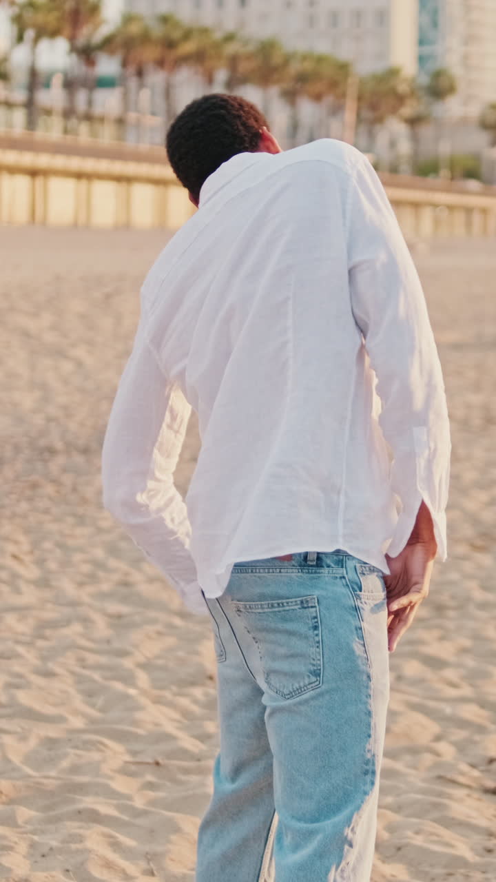 Giovane uomo che danza con espressione su una spiaggia sabbiosa al tramonto