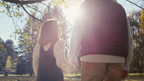 rear view of caucasian little girl walking with grandfather in the par