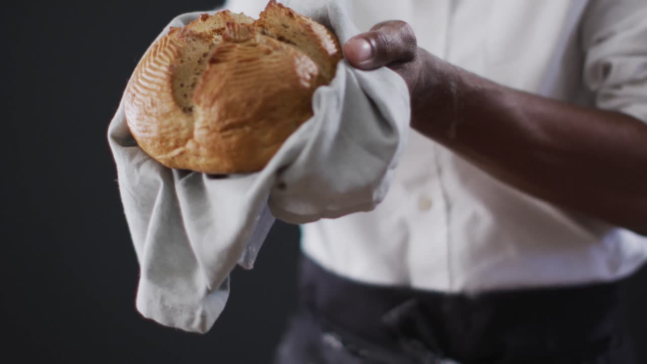 Video of cook holding loaf of bread on black background
