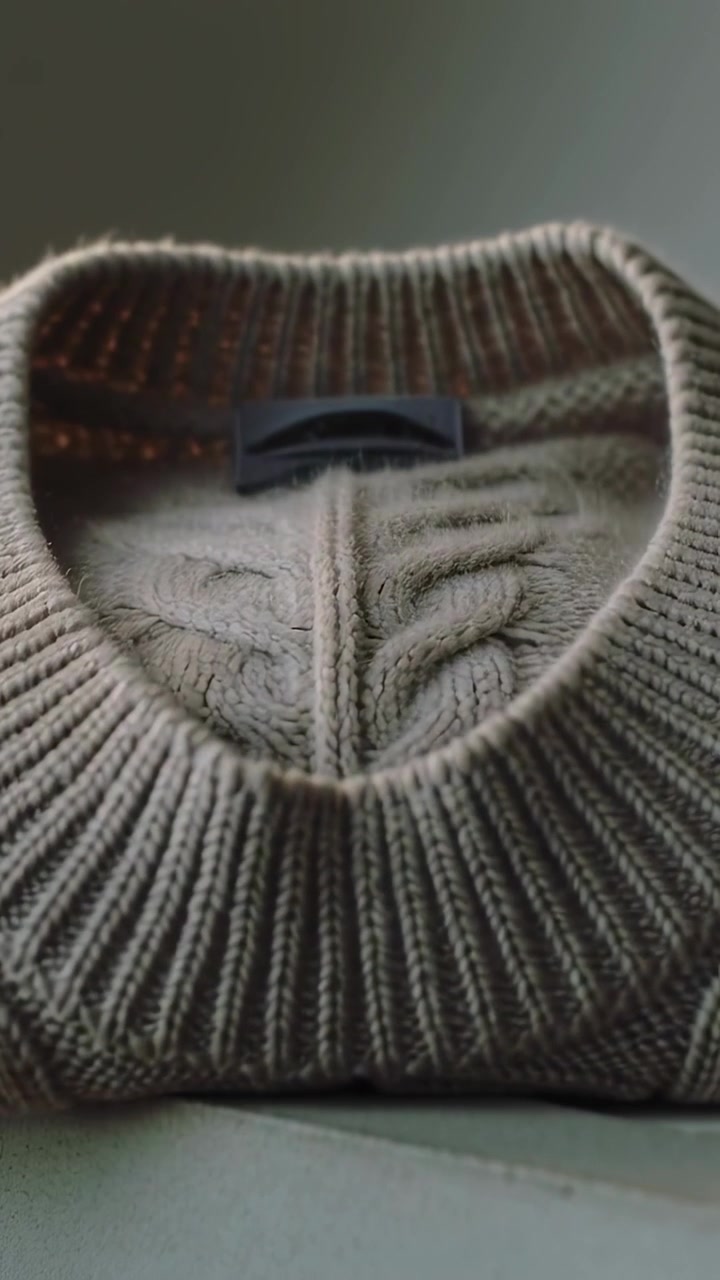 Vertical video: Pulling back camera showing folded ribbed sweater on laptop table, revealing label