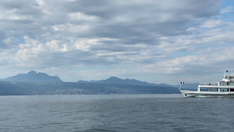 A-tourism-boat-is-crossing-the-frame,-navigating-on-the-Geneva-lake,-biggest-lake-in-west-Europe,-beautiful-view-on-the-French-alps