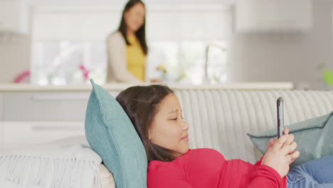 Video-of-happy-asian-girl-resting-on-sofa-with-smartphone