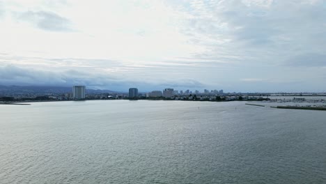 from a distant aerial view, the drone slowly zooms in on emeryville marina park’s waterfront apartments, buildings, and boats.