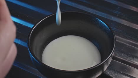 hand pouring and mixing together yogurt and ketchup to make sauce in a black bowel