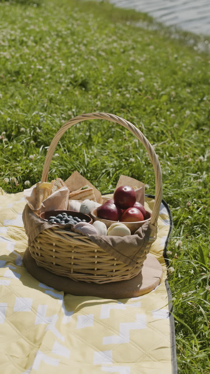 Picnic basket with food on a blanket in a grassy field by a lake