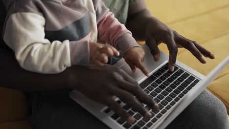 father and small boy typing together on laptop at home on sofa