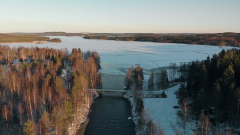 aerial, drone shot, above a river, over a bridge, towards a frozen lake, surrounded by leafless forest and first snow on the ground, on a sunny, autumn day, near joensuu, north karelia, finland